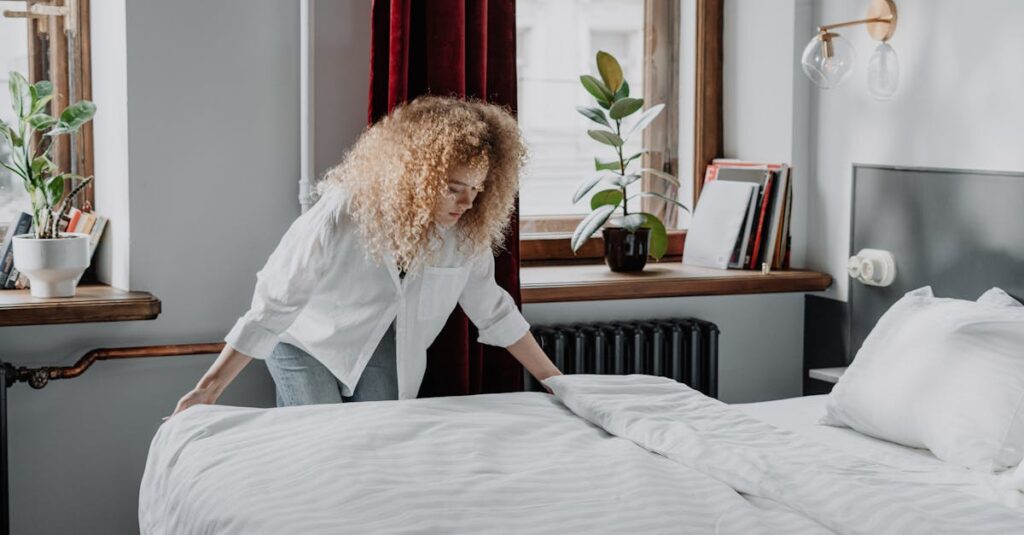 A woman with curly hair making a bed in a bright, cozy bedroom with plants and natural light.